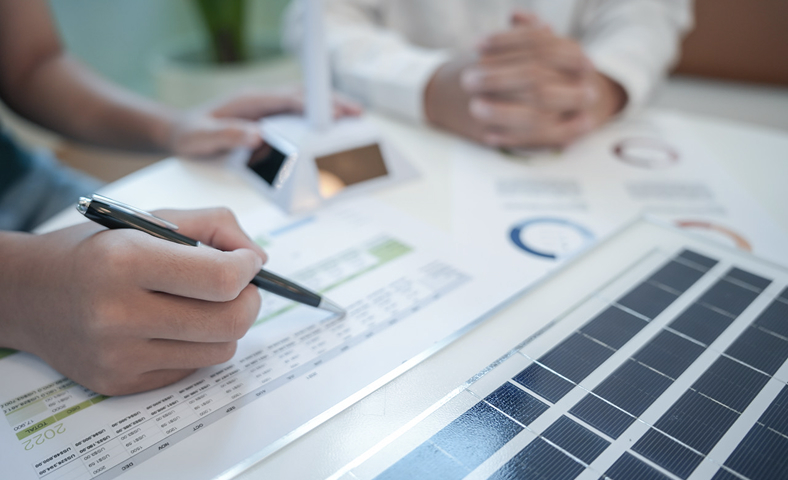 Close-up of a person analyzing solar energy investment data with a miniature solar panel on the desk.