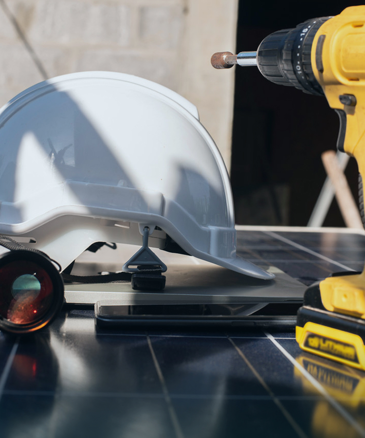 Solar installation tools including a safety helmet, drill, binoculars, and tablet placed on photovoltaic panels at a construction site.