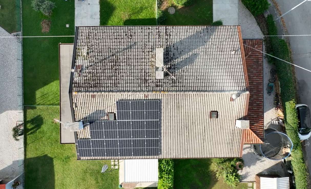 Top-down view of a residential house with rooftop solar panels neatly installed on one side of a tiled roof, surrounded by green lawns and nearby driveway