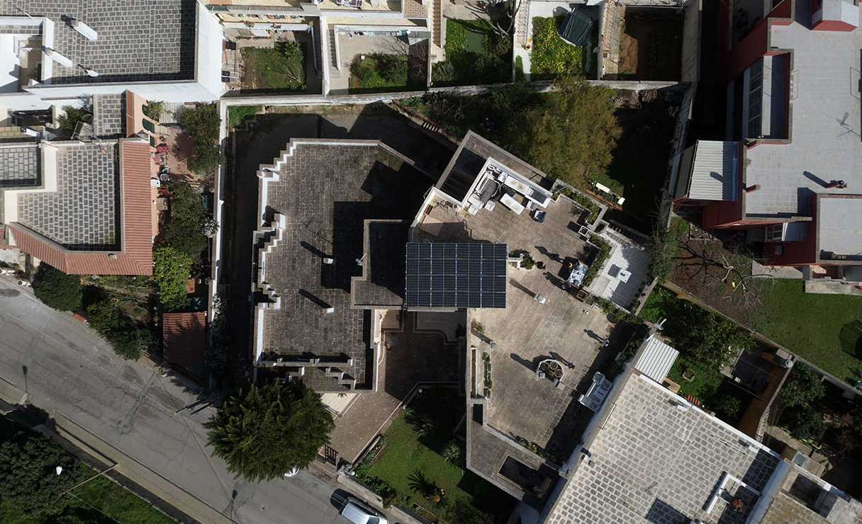 Aerial view of a large city villa with solar panels neatly installed in the central area of the rooftop, surrounded by other residential buildings in a densely populated urban neighborhood