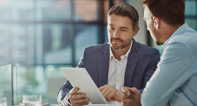 Two business professionals discussing project details using a digital tablet in a modern office setting.