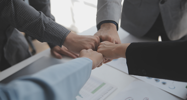 Five business team members fist bumping over desk, symbolizing unity, teamwork and strong partnership.