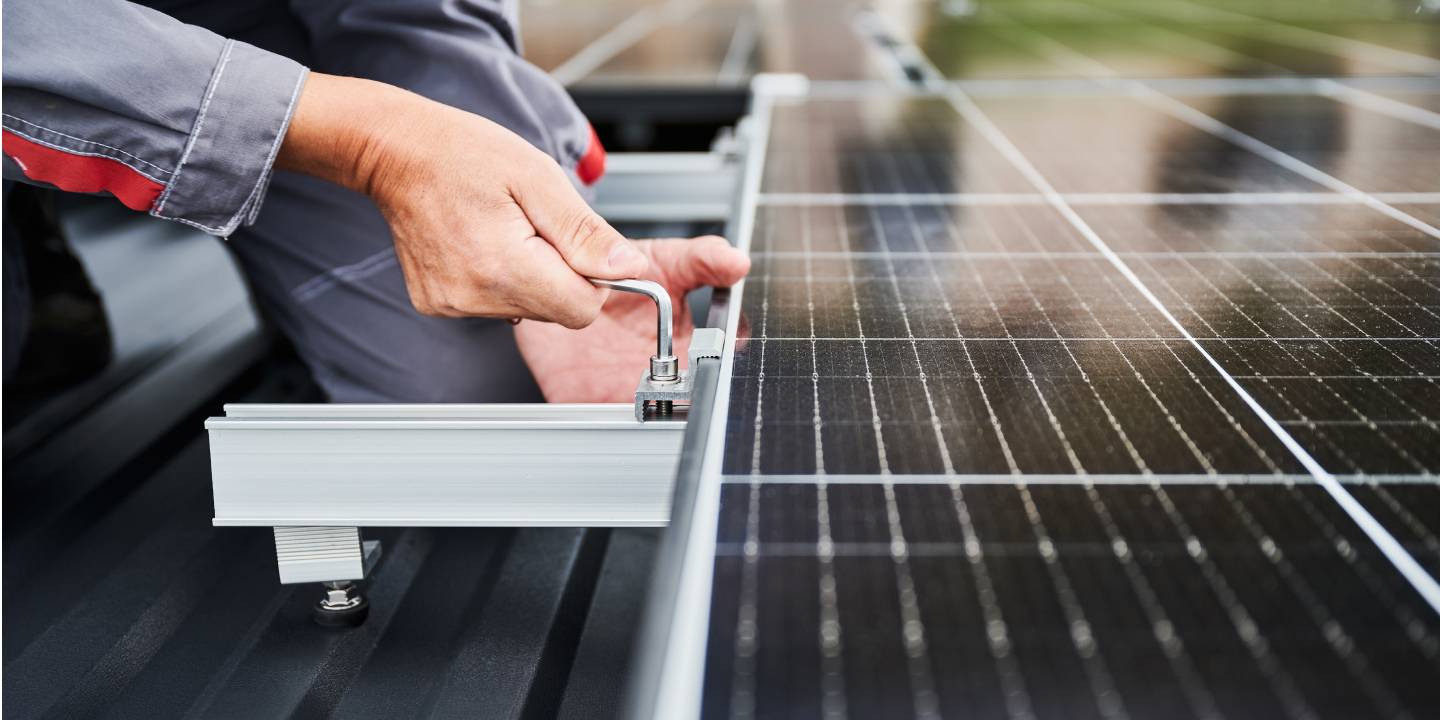 Technician using wrench to install solar panel on metal roof rack