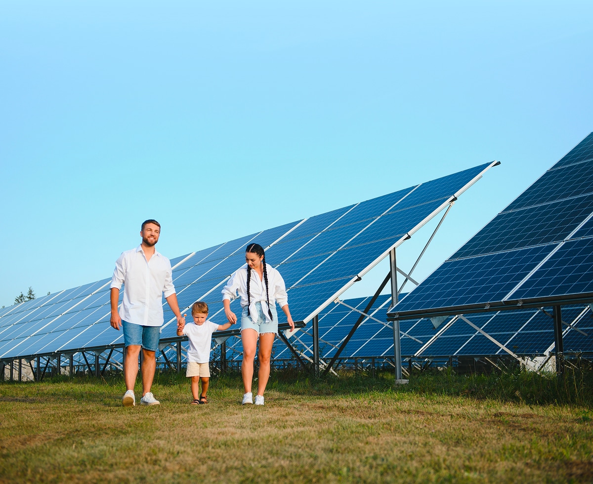 Happy family walking in front of ground-mounted solar panels under clear blue sky, promoting clean energy and a sustainable lifestyle