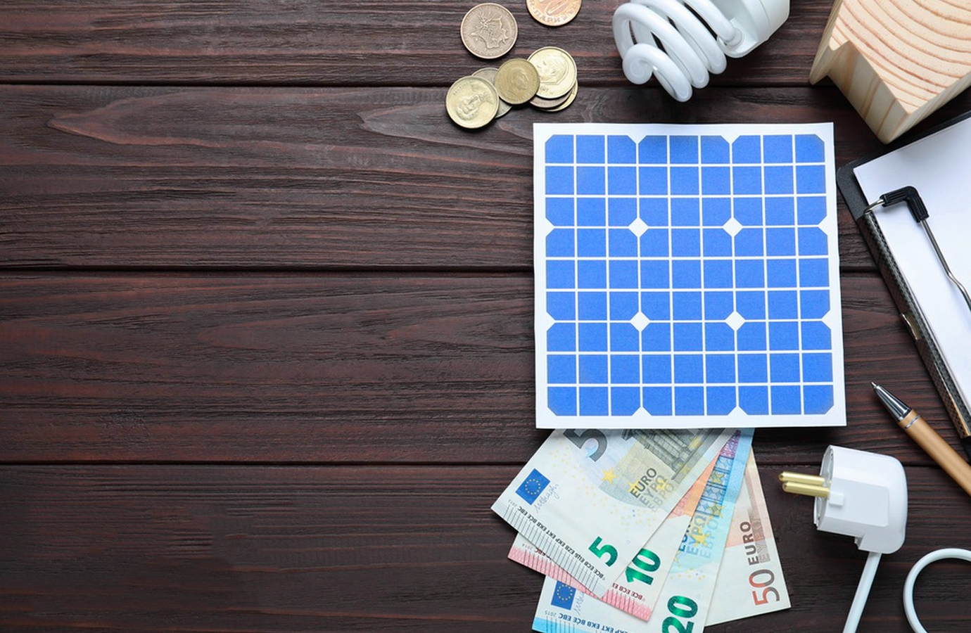 Solar panel, coins, and euro banknotes on a wooden surface, symbolizing savings and energy efficiency with solar power